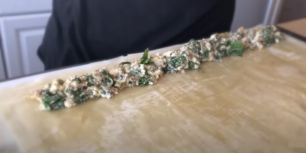 Spinach Feta Borek lays out a row of spinach feta and olive spread with a person standing in the background with a black shirt.