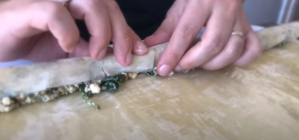 Spinach Feta Borek rolling up spinach feta and olive-filled dough with a person standing in the background with a black shirt.