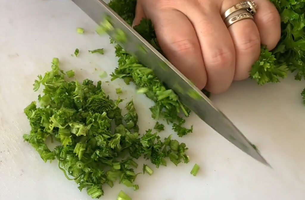 Tabbouleh - Healthy Salad chopping parsley with a knife on a white chopping board.