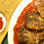 Beef Cutlets in Tomato Marinara Sauce on a white plate with tomato sauce at the bottom with a wooden chopping board and Italian seasoning sprinkled on the background