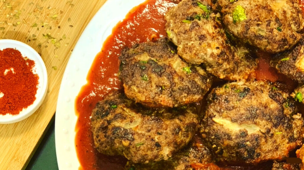Beef Cutlets in Tomato Marinara Sauce on a white plate with tomato sauce at the bottom with a wooden chopping board and italian seasoning sprinkled on the background