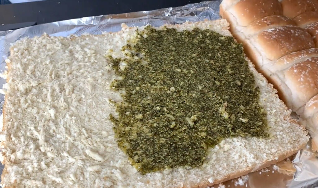 Hawaiian rolls are cut in half on a piece of foil on a black tabletop.