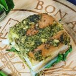 Basil Pesto Swiss bite on a wooden chopping board that says Bon Appitite with a carved wooden board with fresh basil in a jar in the background.