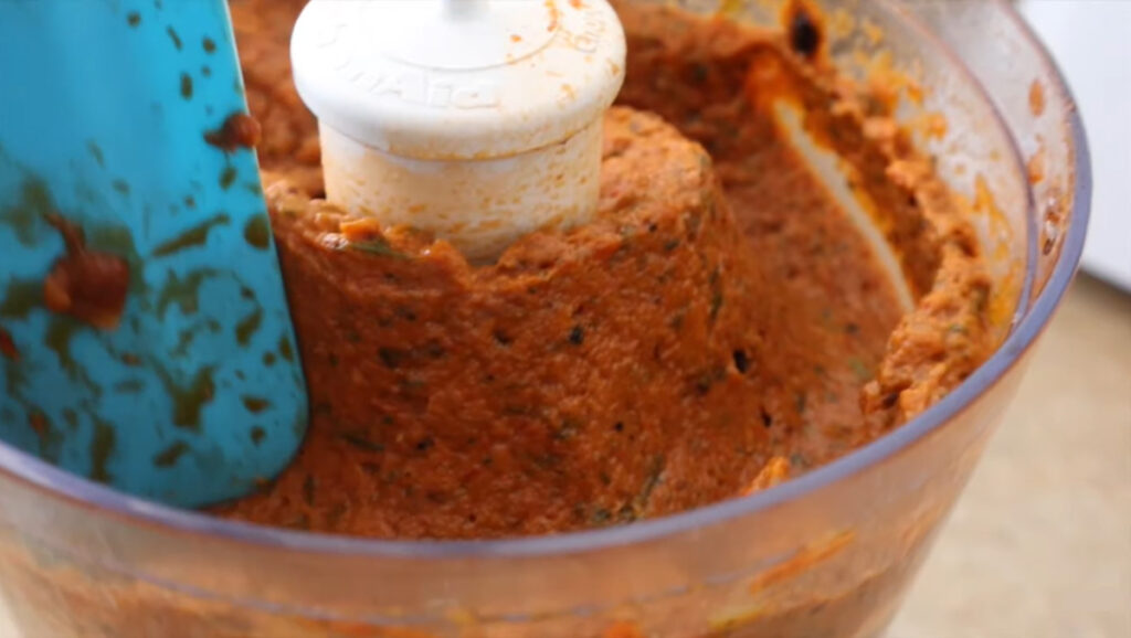 Blended pure eggplant spread in a kitchen aid good processor with a blue rubber spatula.