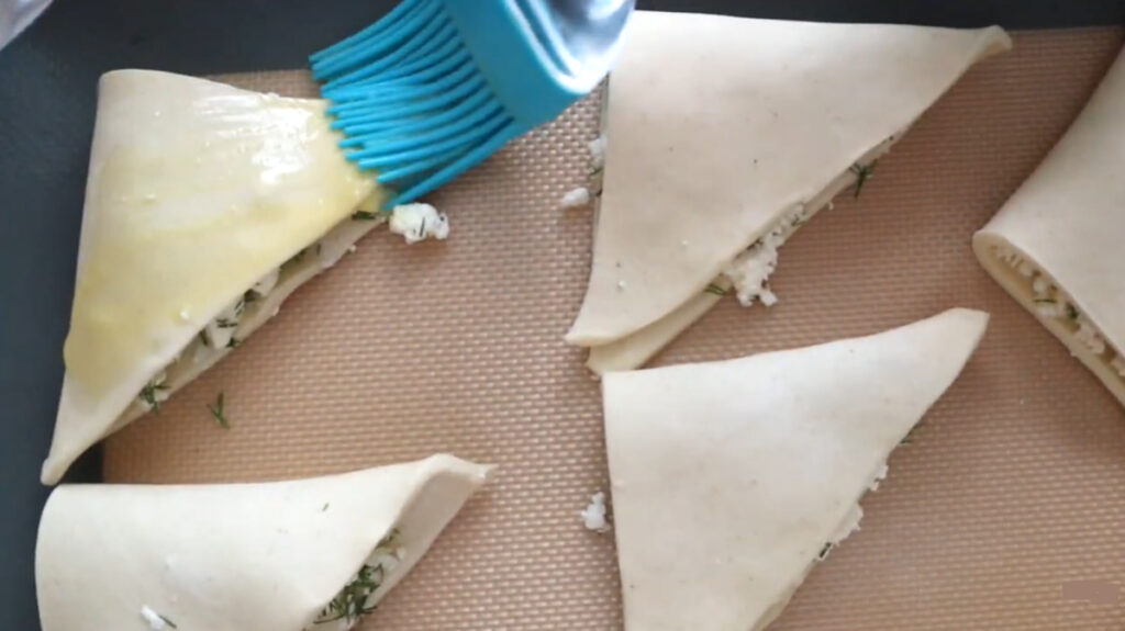 puff pastry dough brushed with egg wash with a blue rubber cooking brush on a baking sheet with a rubber baking mat.
