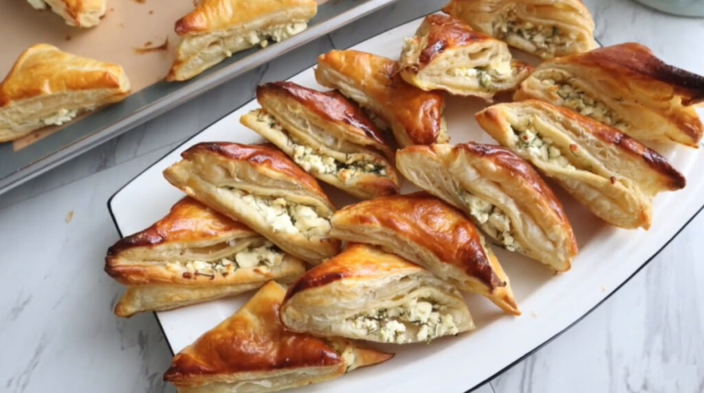 Buttery Cheese Puff Pastry Bites - Borek on a white platter with a baking pan with more Nutella in background