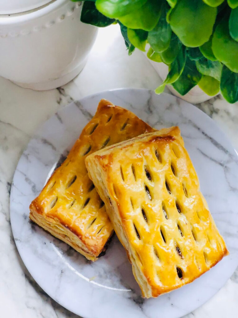 Nutella Walnut Puff Pastry Dessert on a white marble-looking plate with a white canister and a green plant in a white vase on a white countertop.