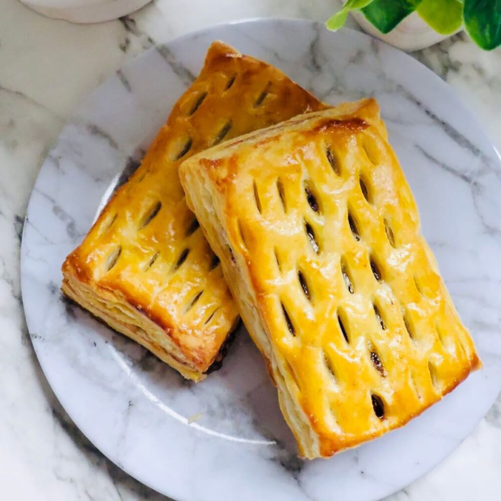 Nutella Walnut Puff Pastry Dessert on a white marble-looking plate with a white canister and a green plant in a white vase on a white countertop.