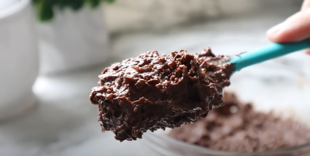 Nutella Walnut Puff Pastry Dessert with a glass bowl in the background with nuts spread on a spoon on a white countertop.