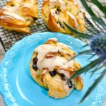 Blueberry Danish Twist Brioche Bread Dessert on a black cooling rack on a white marble counter with white canisters with a canister full of flour accented with blue thistle flower.