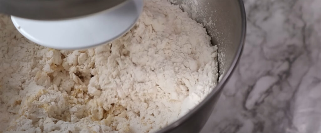 Blueberry Danish Twists flour in a mixing bowl attached to an electric mixer on a white countertop.