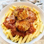 Cajun Chicken Meatball Pasta in a white pasta bowl with a grey towel around the plate as accent decor.