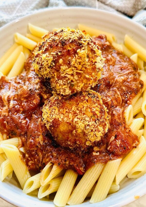 Cajun Chicken Meatball Pasta in a white pasta bowl with a grey towel around the plate as accent decor.