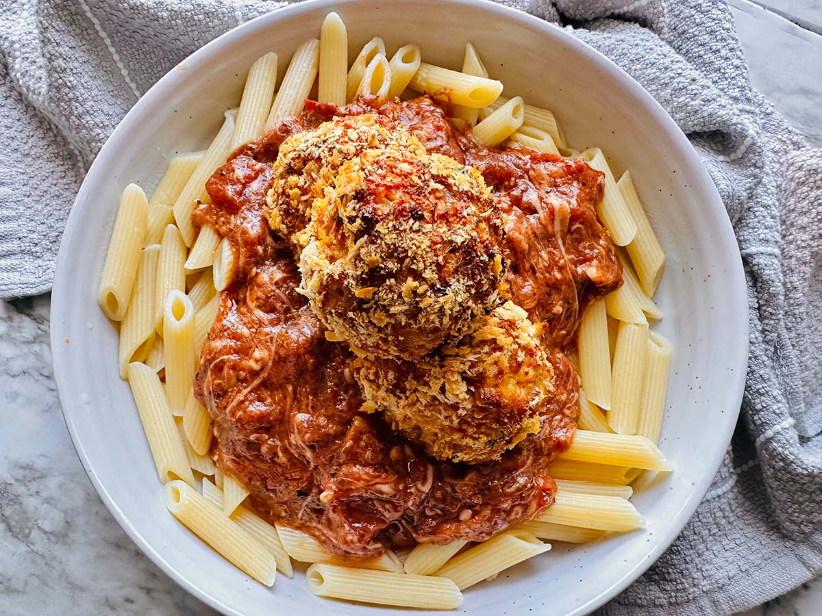 Cajun Chicken Meatball Pasta in a white pasta bowl with a grey towel around the plate as accent decor.