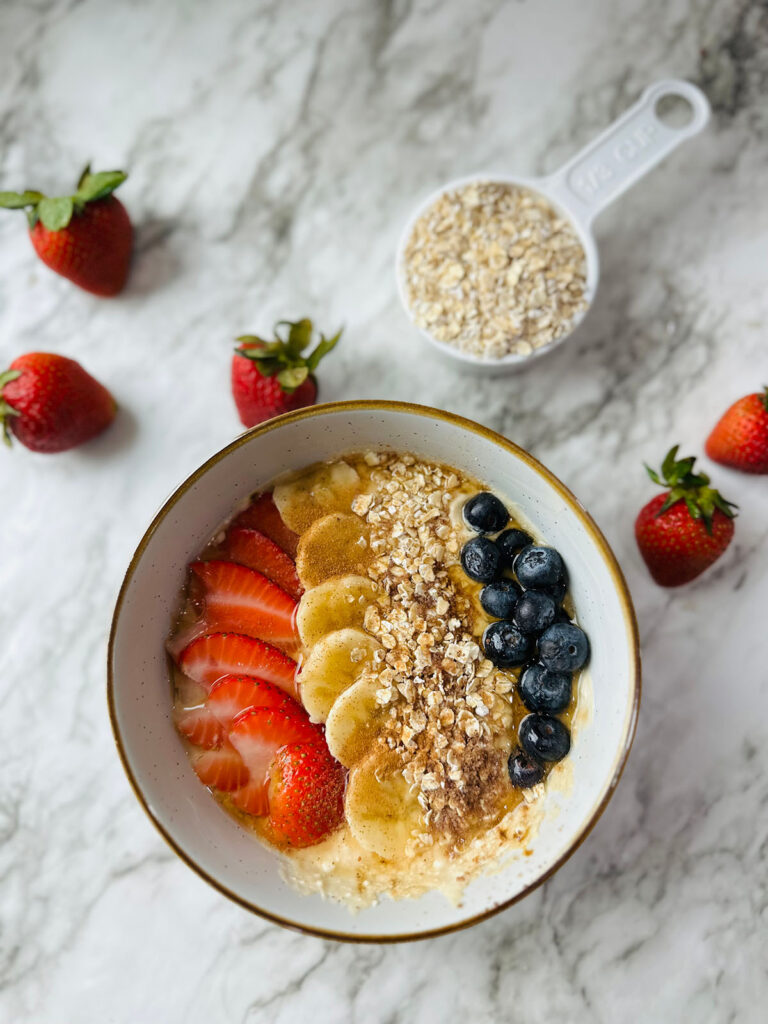Healthy Mocha Coffee Yogurt in a bowl with fresh strawberries and cracked oats in a measuring cup on a white countertop
