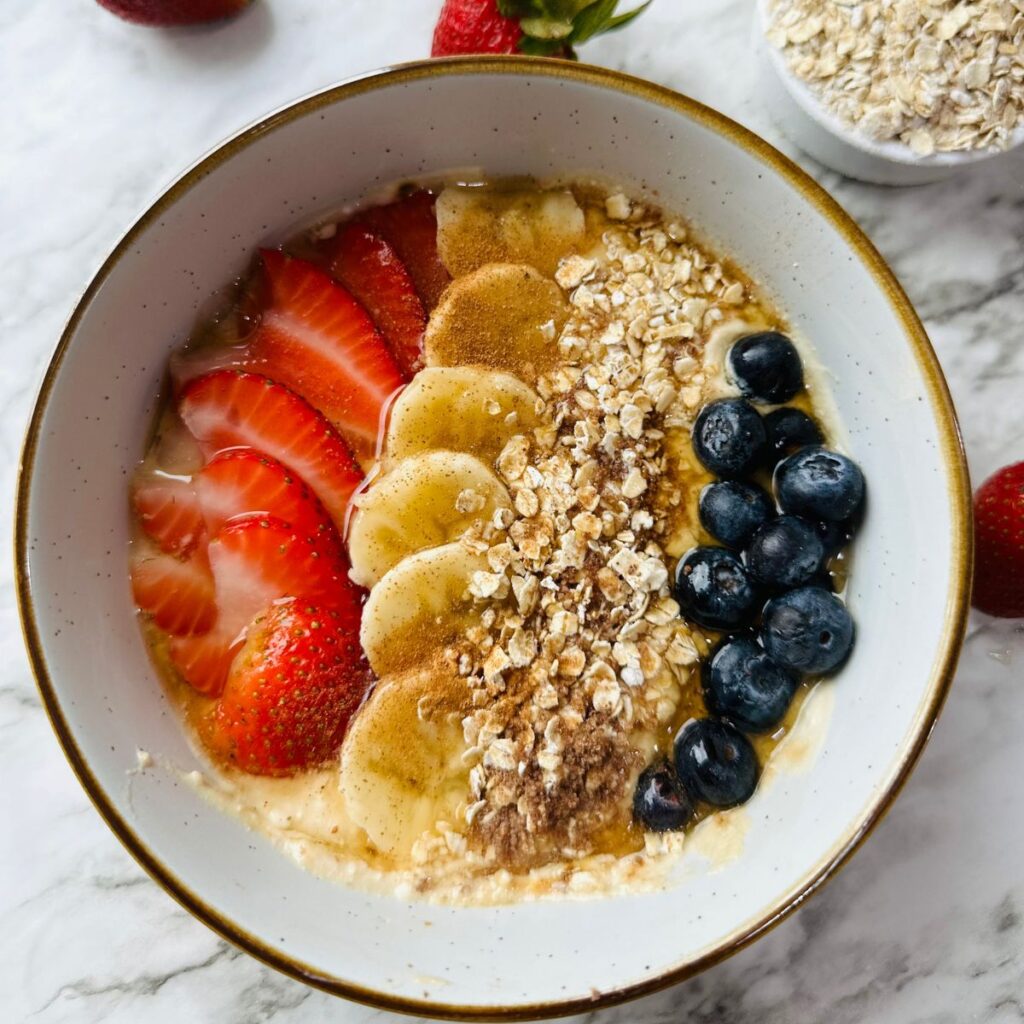 Healthy Mocha Coffee Yogurt in a bowl with fresh strawberries and cracked oats in a measuring cup on a white countertop
