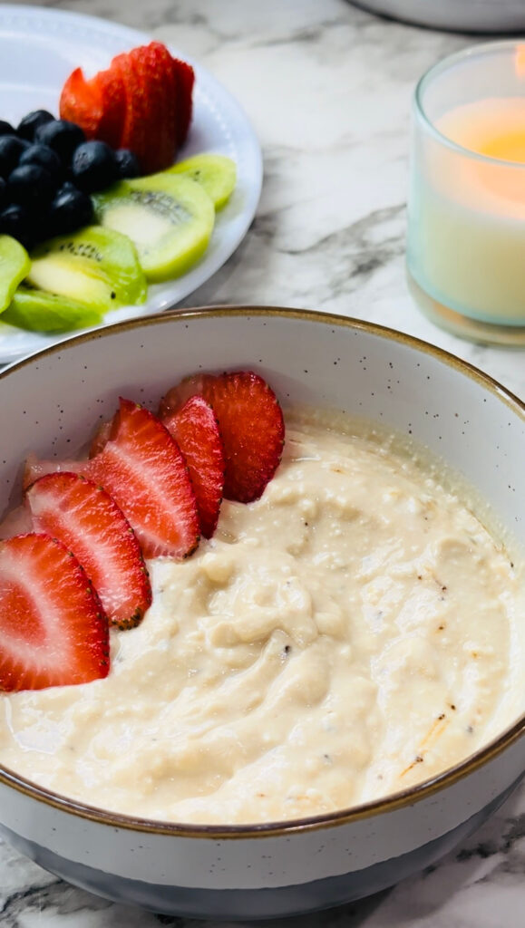 Healthy Mocha Coffee Yogurt yogurt with decorated straberries placed around the edge of the bowl with a plate of fruits and a lit candle in the background on a white countertop with white vases in the background.