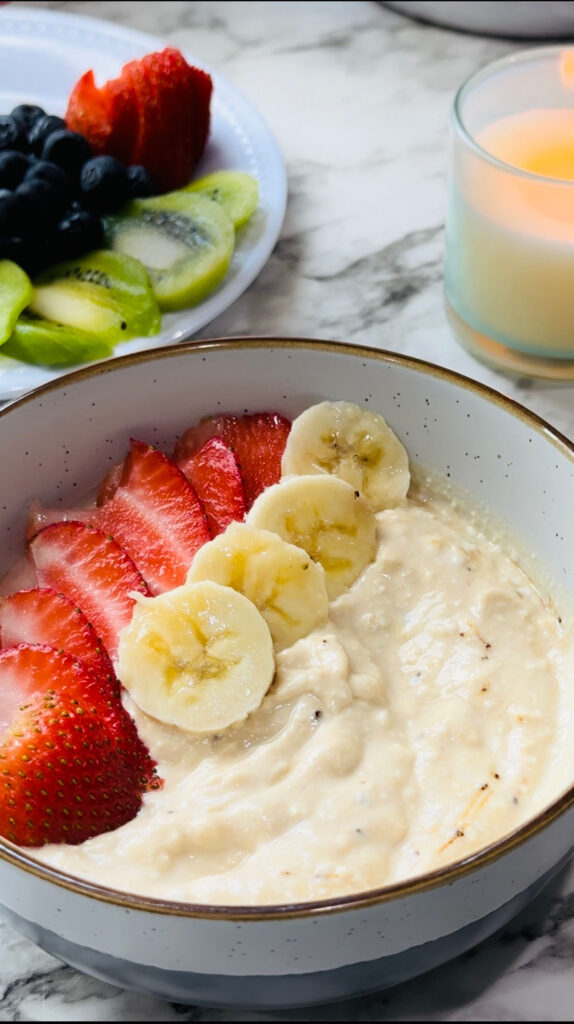 Healthy Mocha Coffee Yogurt yogurt with decorated strawberry and banana slices placed around the edge of the bowl with a plate of fruits and a lit candle in the background on a white countertop with white vases in the background.