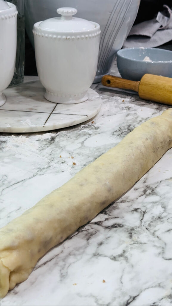 Walnut Roll Pastry Rolled up ready to cut on top of a white countertop with white canisters and a wooden rolling pin on the counter.
