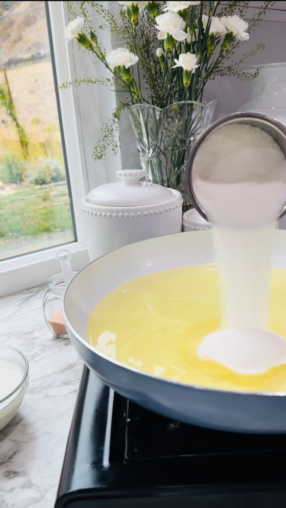 Walnut Roll Pastry with a blue and white cooking pan melting crisco shortening pouring sugar into pan with a glass bowl of oil on a white countertop in front of a kitchen window.