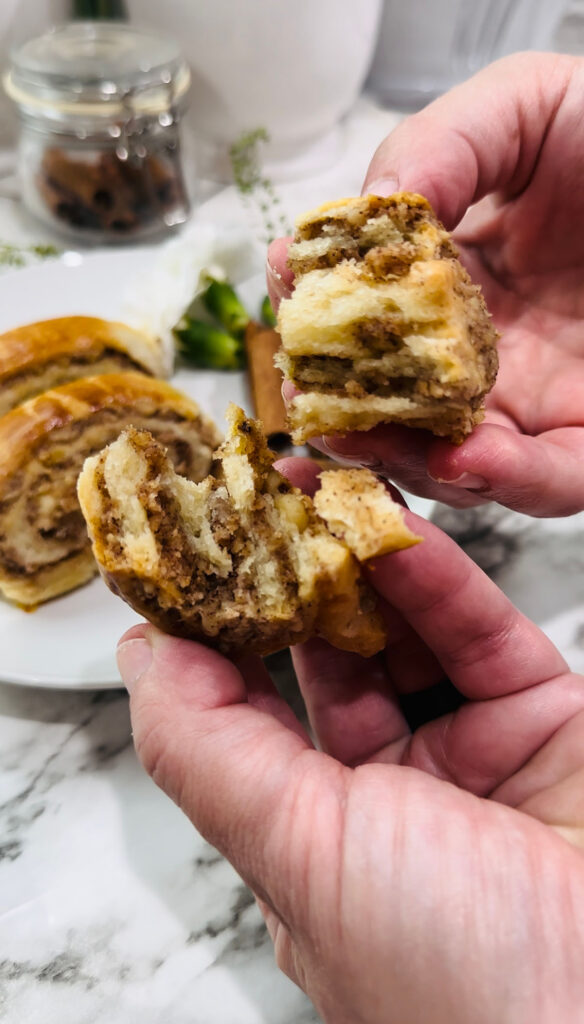 Walnut Roll Pastry all done split in half with hands showing inside of the roll with a white plate with walnut rolls ontop of plate on a white countertop