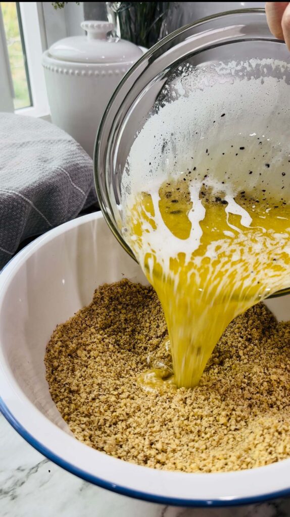 Walnut Roll Pastry - crushed walnuts in a bowl pouring melted butter into walnuts in a ceramic bowl with white canisters on a white granite countertop