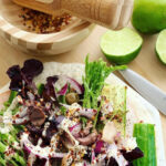 Low-carb wraps with cut limes a wooden mortar grinder on a white plate on a wooden chopping board.