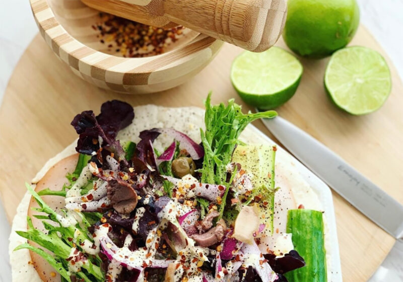 Low-carb wraps with cut limes a wooden mortar grinder on a white plate on a wooden chopping board.