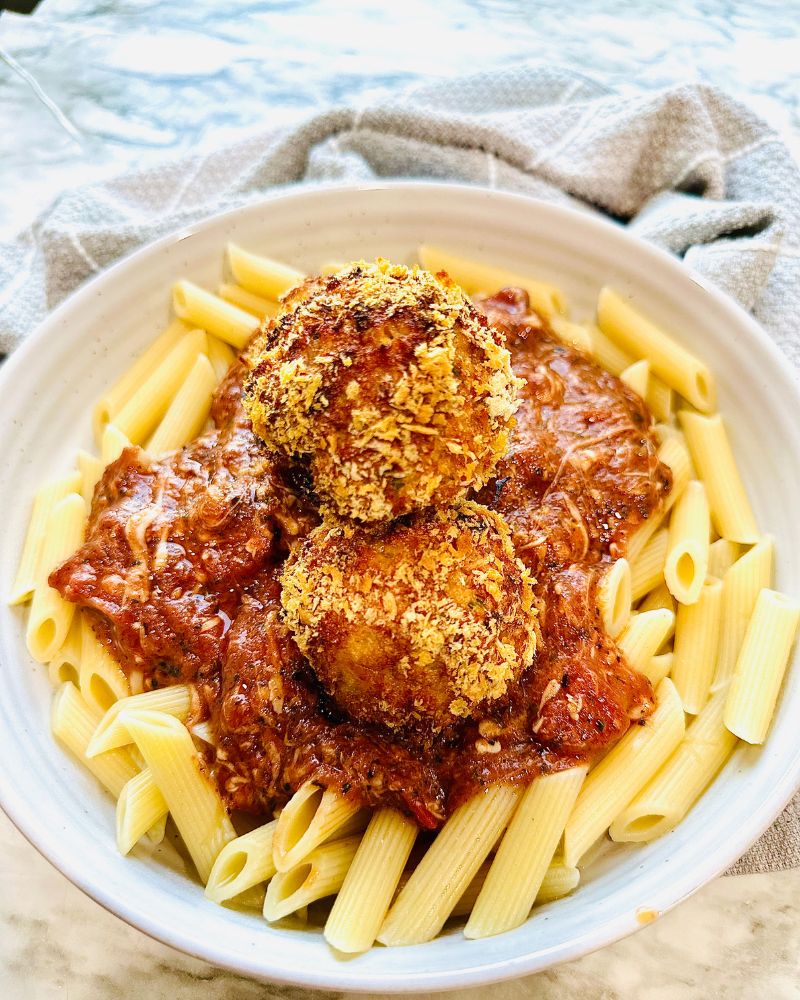 Cajun Chicken Meatball Pasta in a white pasta bowl with a grey towel around the plate as accent decor.