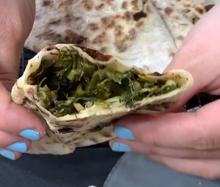 Zhingylov Hats - Fresh Greens in a Homemade Flatbread - Cut zhingylov hats in half and showing the filling inside holding with two hands