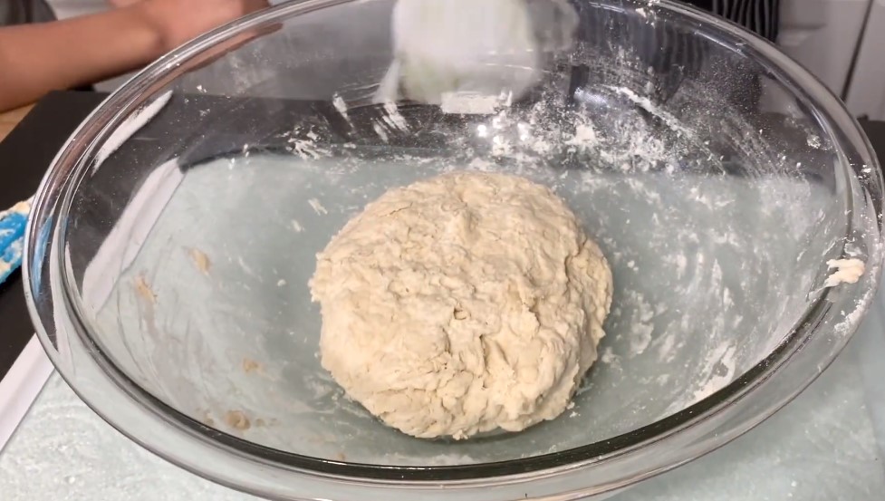 Fresh Greens in a Homemade Flatbread - Dough with sour cream in a glass bowl on a black countertop with a black and white stripped apron in background
