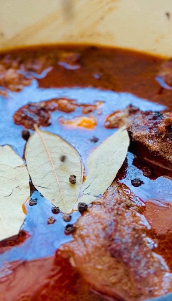 Beef covered with beef broth, 3 bay leaves and pepper corn ontop of broth in a white stone pot