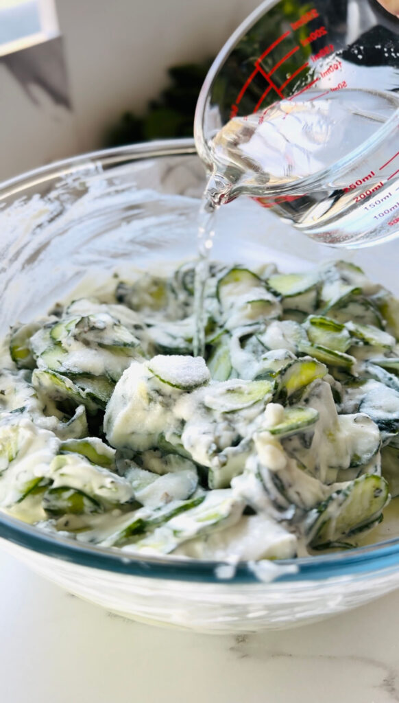 Jajukh | Refreshing Yogurt Salad with Cucumbers and Mint mixed salad adding salt and water with a small glass measuring cup filled with water. 