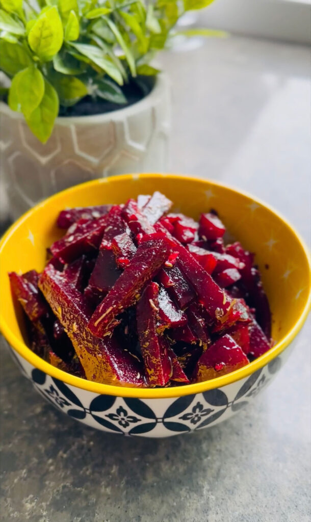Simple Sweet / Sour Vinaigrette Beet Salad in a yellow bowl with black and white decor around the outside of the boal with a grey pot with a green plant in background on a black marble counter.