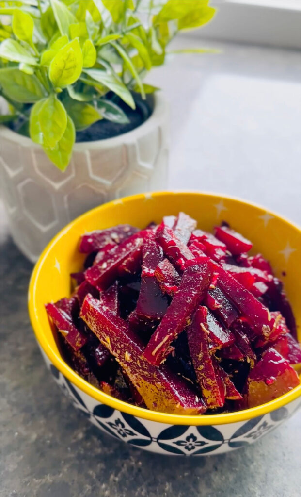 Simple Sweet / Sour Vinaigrette Beet Salad in a yellow bowl with black and white decor around the outside of the boal with a grey pot with a green plant in background on a black marble counter.