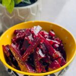 Simple Sweet / Sour Vinaigrette Beet Salad in a yellow bowl with black and white decor around the outside of the boal with a grey pot with a green plant in background on a black marble counter.