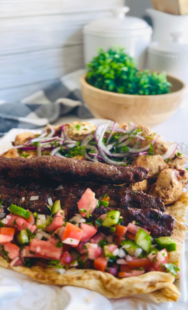 4 Best Wrap Recipes | Perfect Lunch or Dinner Ideas- So easy to make and good! Beef and Lamb lule kebob with chicken kebob skewers with fresh tomato and cucumber herb salad ontop of lavash bread with sliced onions with sumac with a wooden bowl and green fern in background with a grey and white towel accenting table.