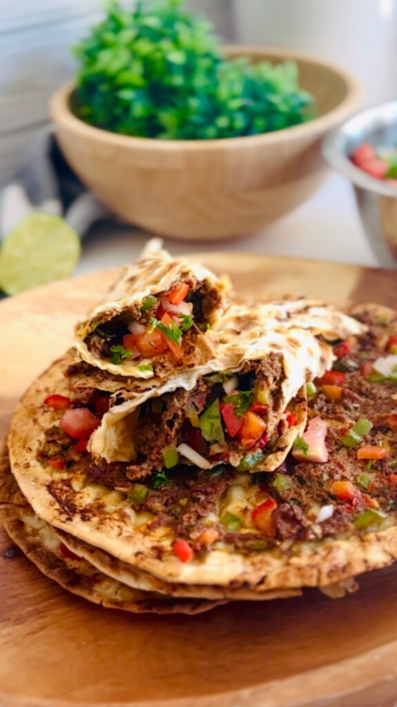 4 Best Wrap Recipes | Perfect Lunch or Dinner Ideas-  So easy to make and good! Minced Beef and Lamb meat baked ontop of a lavash wrap with fresh herbs, spices and vegetables.  On top of a wooden wround board, with a wooden bowl in background with a slice of lemon in background.