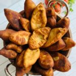 Potato Pirashki / Piroshki wooden bowl with silver handles in fried Pirashki's with fresh tomatoe and cilantro in background.