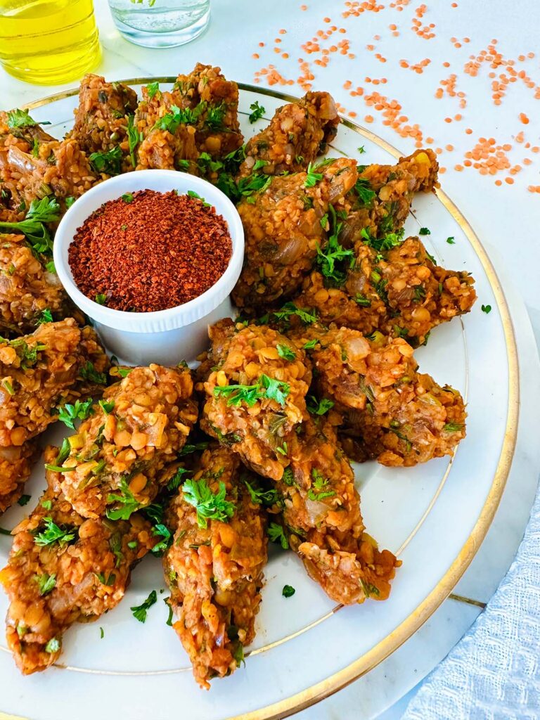 Vegan Red Lentil Kofte (Vospov Kofte) on a white platter with a glass oil pitcher with a white oil plate and lentils on white tabletop with white towel