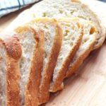 Homemade Fresh Bread Made Easy - Sliced loaf of bread (not scored) ontop of a wooden chopping board with a white stipped kitchen towl and a bread knife on a black countertop.