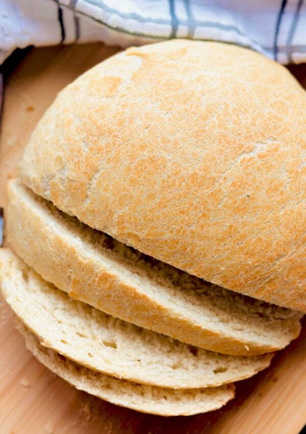 Homemade Fresh Bread Made Easy - Sliced loaf of bread (not scored) ontop of a wooden chopping board with a white stipped kitchen towl and a bread knife on a black countertop.