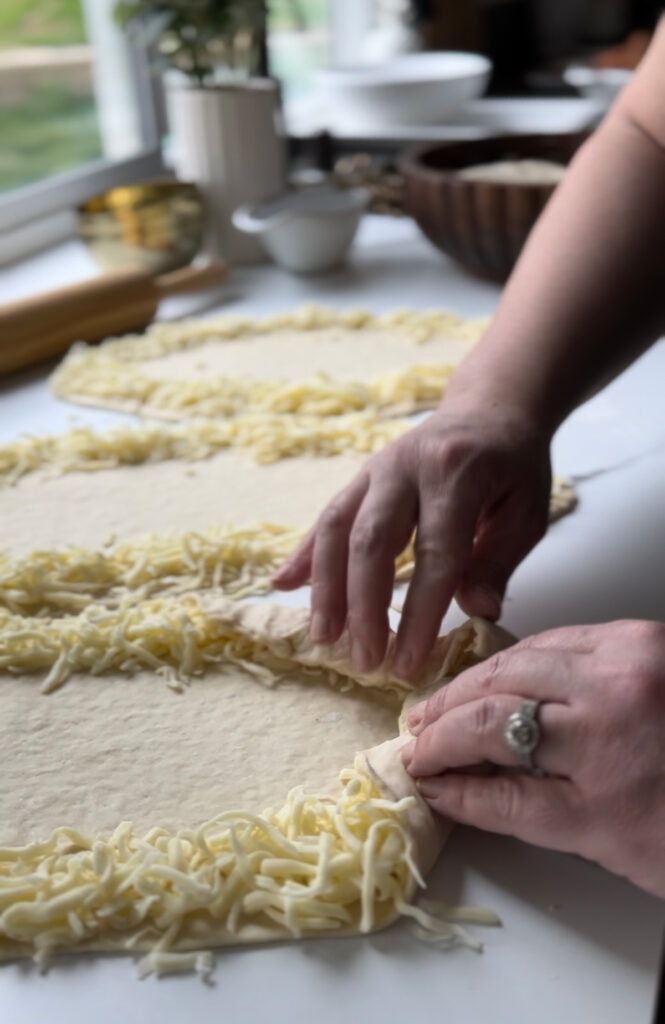 Middle Eastern Meat Flatbreads - dough edges filled with cheese and two hands folding over the dough to close.