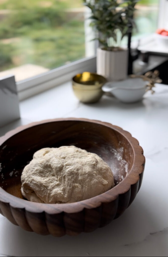 Middle Eastern Meat Flatbreads - wooden bowl filled dough with a wooden tray with white and glass bowls in background with a wooden chopping board on a white countertop