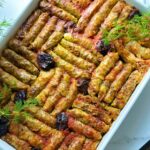 Stuffed Cabbage Leaves Dolma with Prunes in a white baking platter with fresh herb dill cascading ontop as a decor and a wooden chopping board in the top corner.
