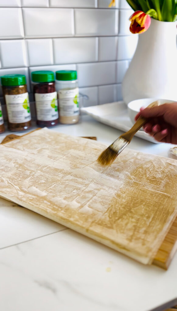Jalapeño Phyllo Poppers with Roasted Pine Nuts - phyllo dough brushing butter over them with seasonings with green lids in background with a white pitcher with fresh tulips in side.