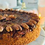 Buttery Pecan Upside Down Cake - Almond Cow - Pecan upside cake cut slice on white plate with fall docor and a lit candle in background with a white pumpkin decor in background.