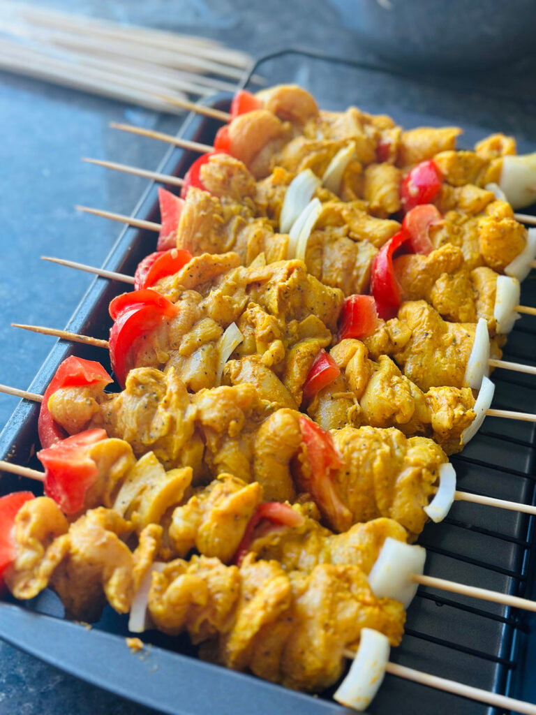 Tender Oven Baked Chicken Kebobs - chicken kebobs in a baking pan skewed in wooden skewers and has chopped red peppers and onions inbetween marinated chicken