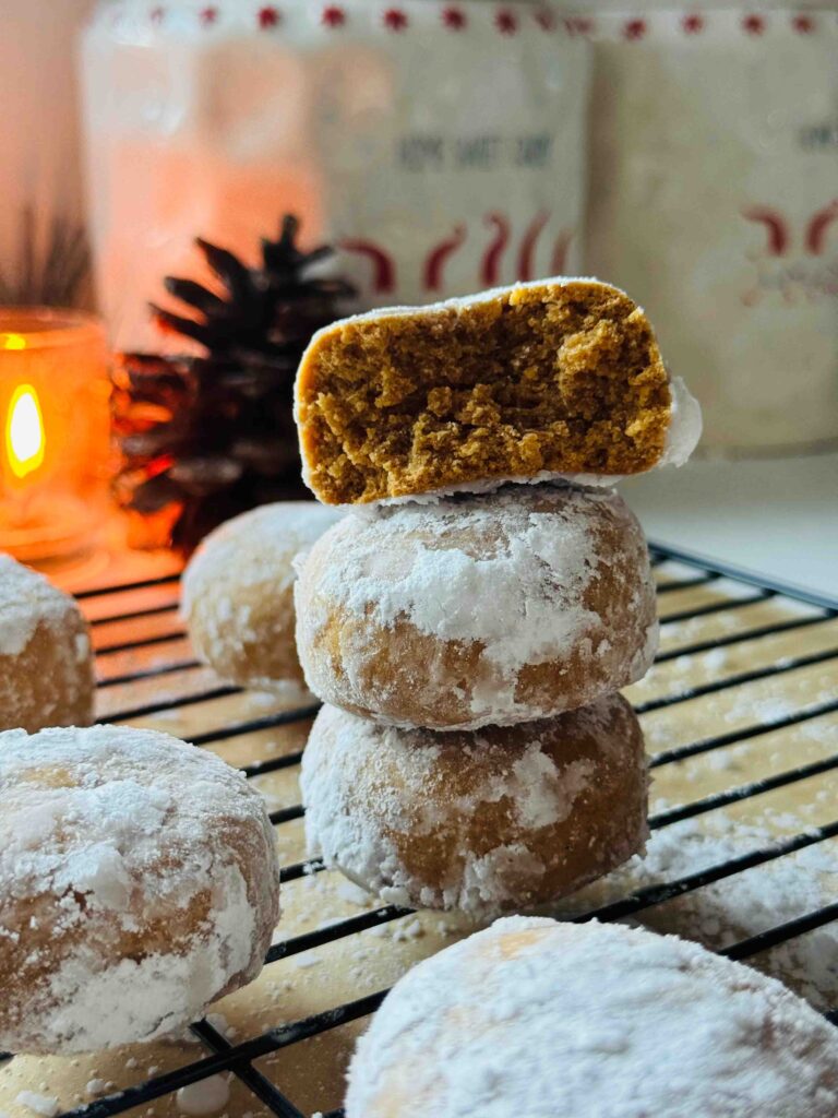 Spiced Holiday Pryaniki Cookies - Ginger Cookies- 3 cookies ontop of eachother with a lit candle in background cookies surrounding on a black cooling rack with two christmas canisters in background