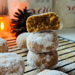 Spiced Holiday Pryaniki Cookies - Ginger Cookies- 3 cookies ontop of eachother with a lit candle in background cookies surrounding on a black cooling rack with two christmas canisters in background